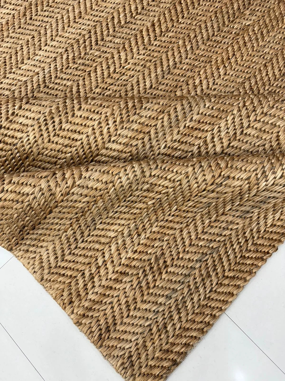 Natural tan jute herringbone area rug styled in a light blue coastal-inspired room