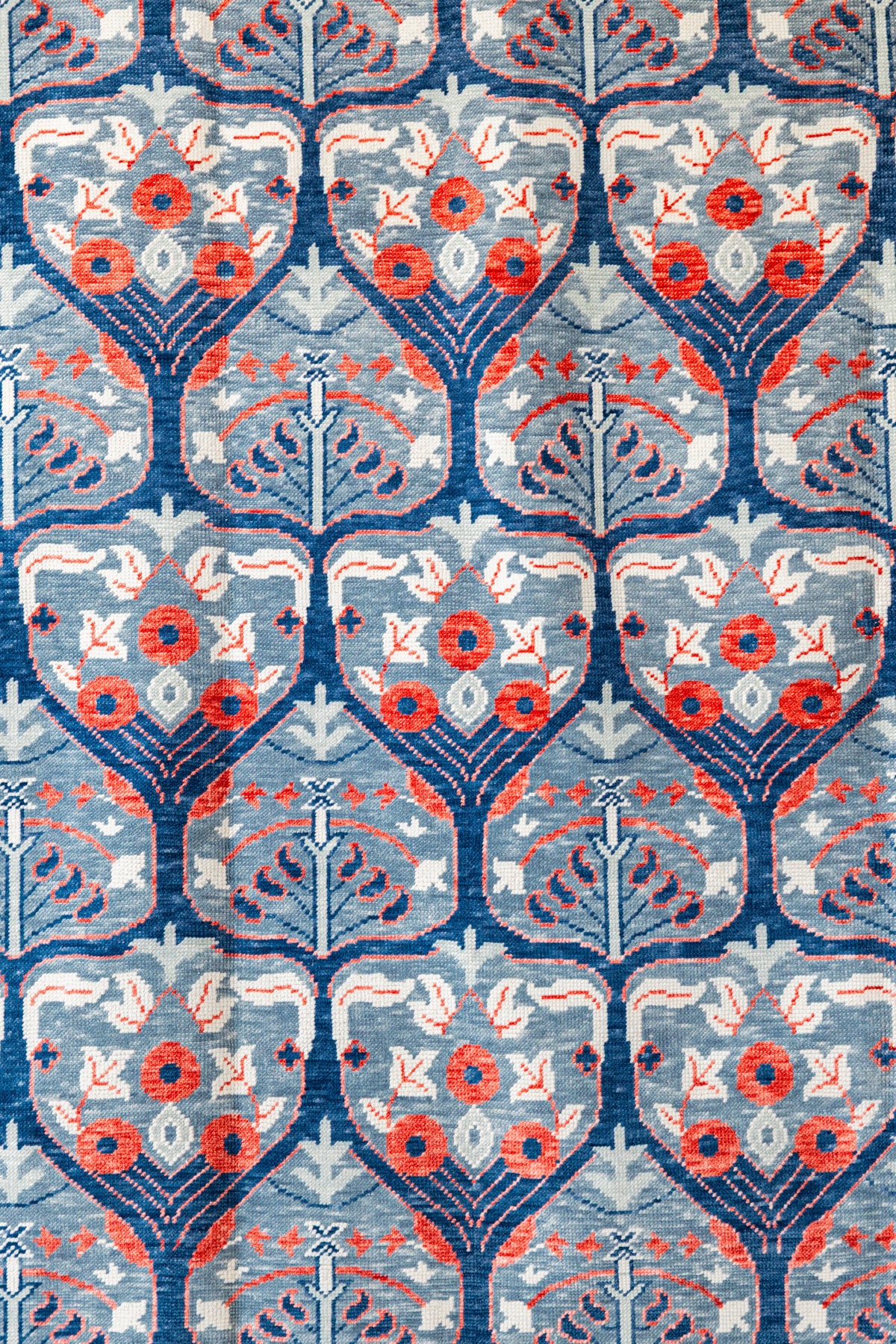 Detailed view of blue red and ivory Modern Oushak rug with repeating stylized botanical floral pattern