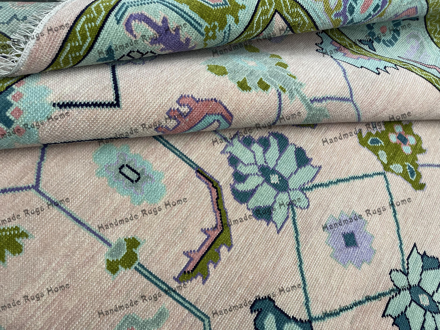 Handmade light pink and green geometric Oushak rug on a wooden floor.
