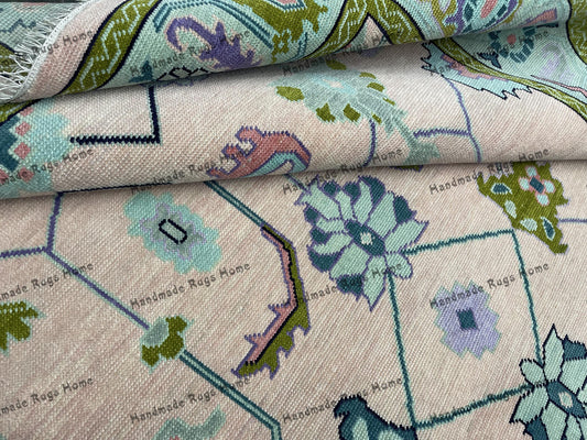 Handmade light pink and green geometric Oushak rug on a wooden floor.