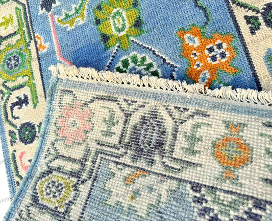Hand-knotted wool Oushak-style rug, rectangular, with a powder blue background and large pastel pink and olive green floral patterns.