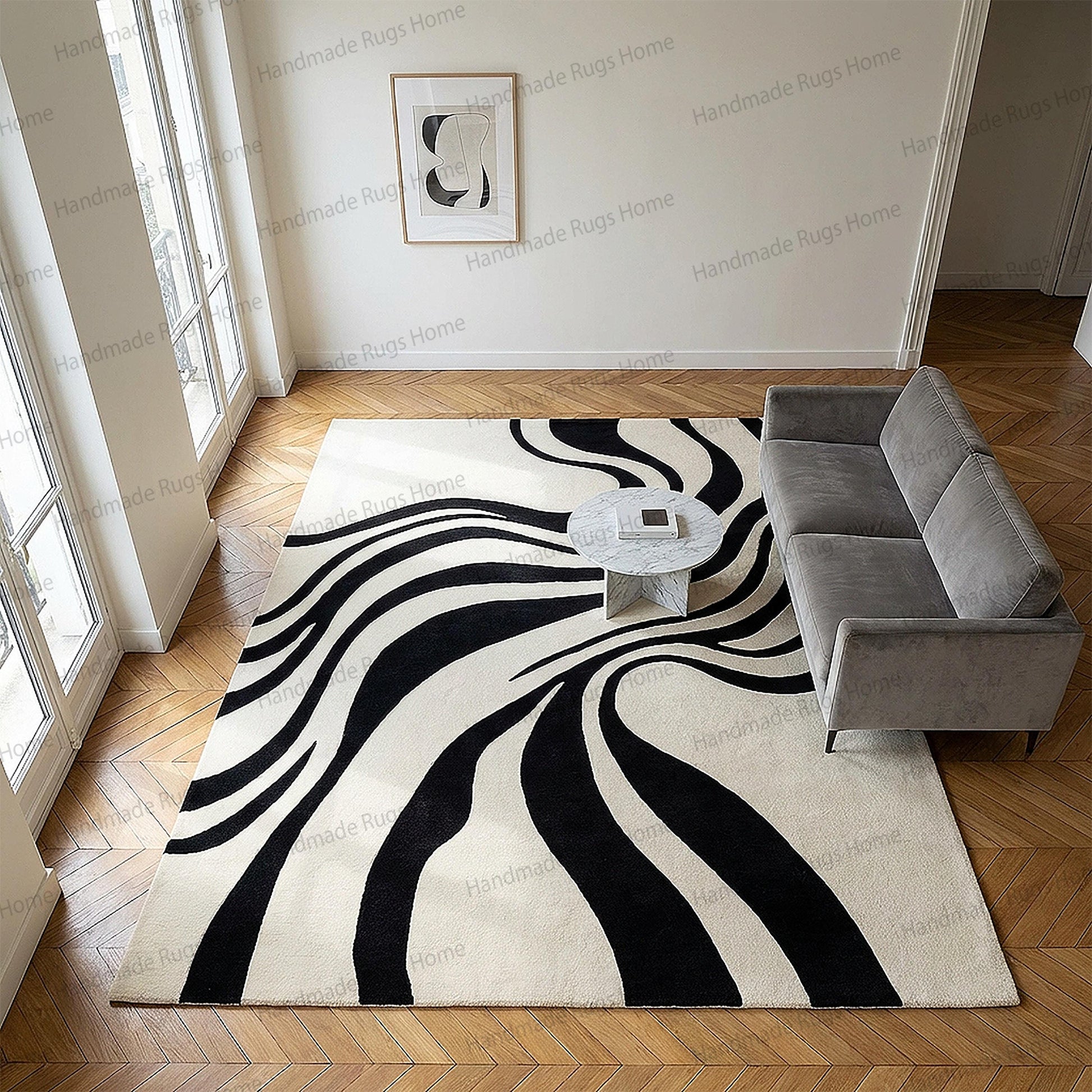 May include: A large, rectangular rug with a bold black and white abstract design. The rug features flowing, wave-like black stripes against a cream-colored background. A gray sofa and marble coffee table are also in the room.