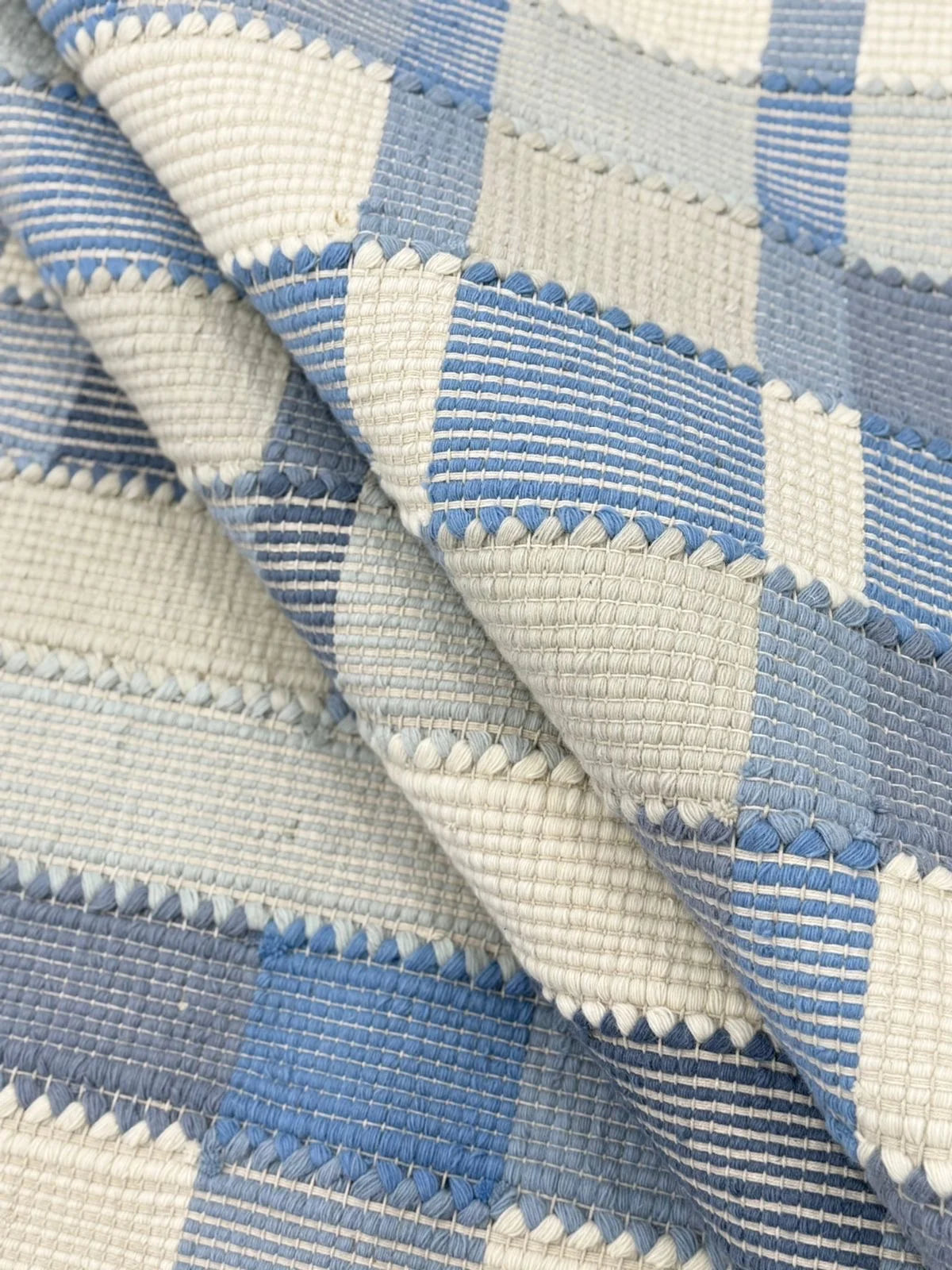 Close-up of blue and ivory flatweave rug showing textured woven plaid and geometric block pattern